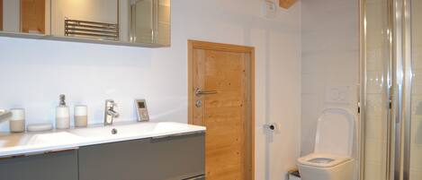 A bathroom with a wooden door, a white sink with a mirror above it, and a toilet with a glass enclosure.