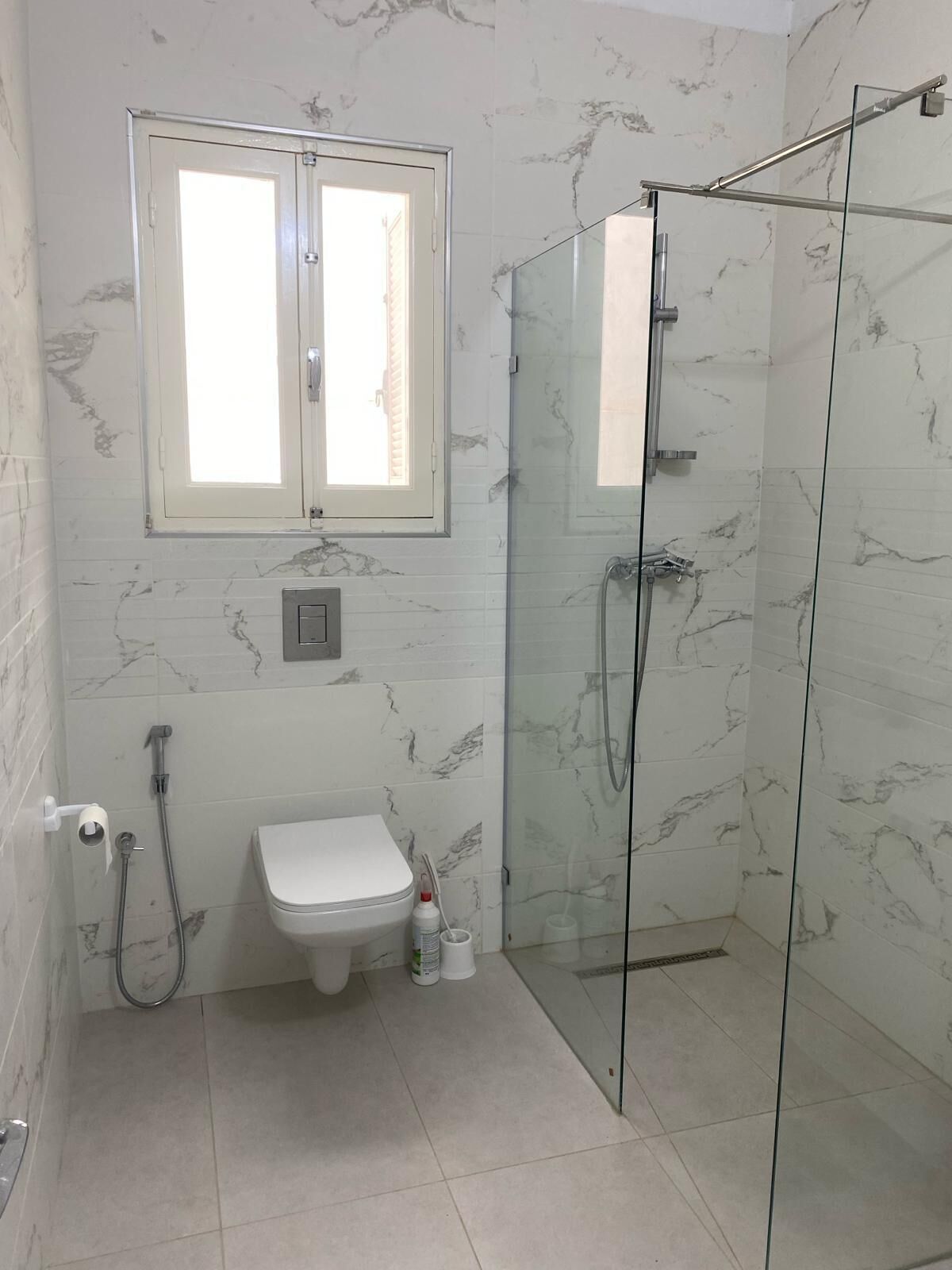 A bathroom with a glass-enclosed shower, a toilet, a sink, and a window above the sink.