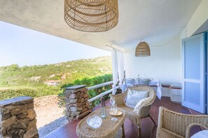 Ein Balkon mit Korbmöbeln, einer Steinmauer und Blick auf Grünflächen.