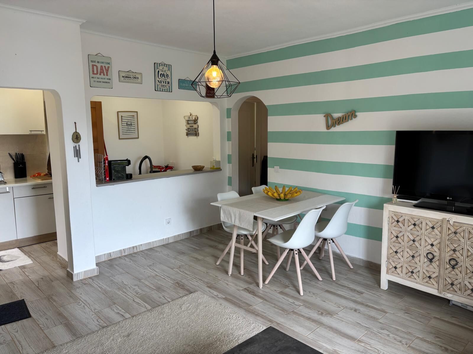 A modern kitchen with a dining area, a TV, and a striped wall.
