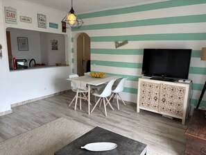 A living room with a dining area, a flat-screen TV, and a kitchen area with a sink and utensils. - The Riscas House—Apartment in Alvor Brisamar (portimao)