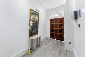 A hallway with a wooden door, a framed painting, and a light fixture. - Oak Lane Studio (London)