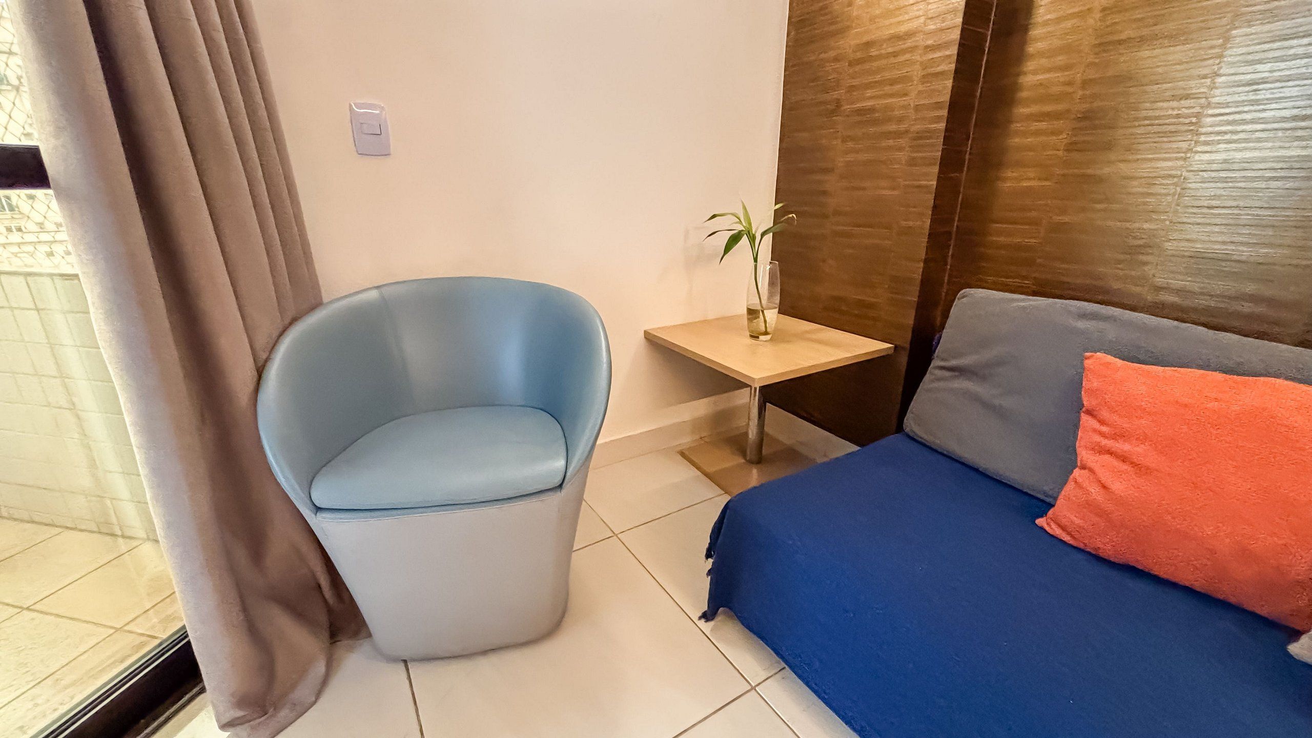 Una habitación con un sofá azul, un sillón azul claro, una pequeña mesa con una planta y una ventana con cortinas.