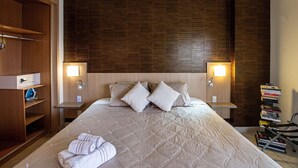Een hotelkamer met een groot bed, twee nachtkastjes, een kledingkast en een stapel boeken.