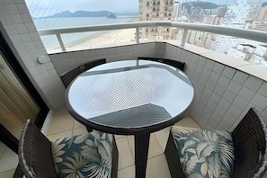 A balcony with a round table and two chairs, a tiled floor, and a view of a beach and buildings. - SHB Magnífica vista ao mar em Santos (Santos)