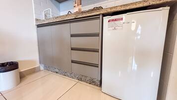 A kitchen with a white refrigerator, a trash bin, and a granite countertop.