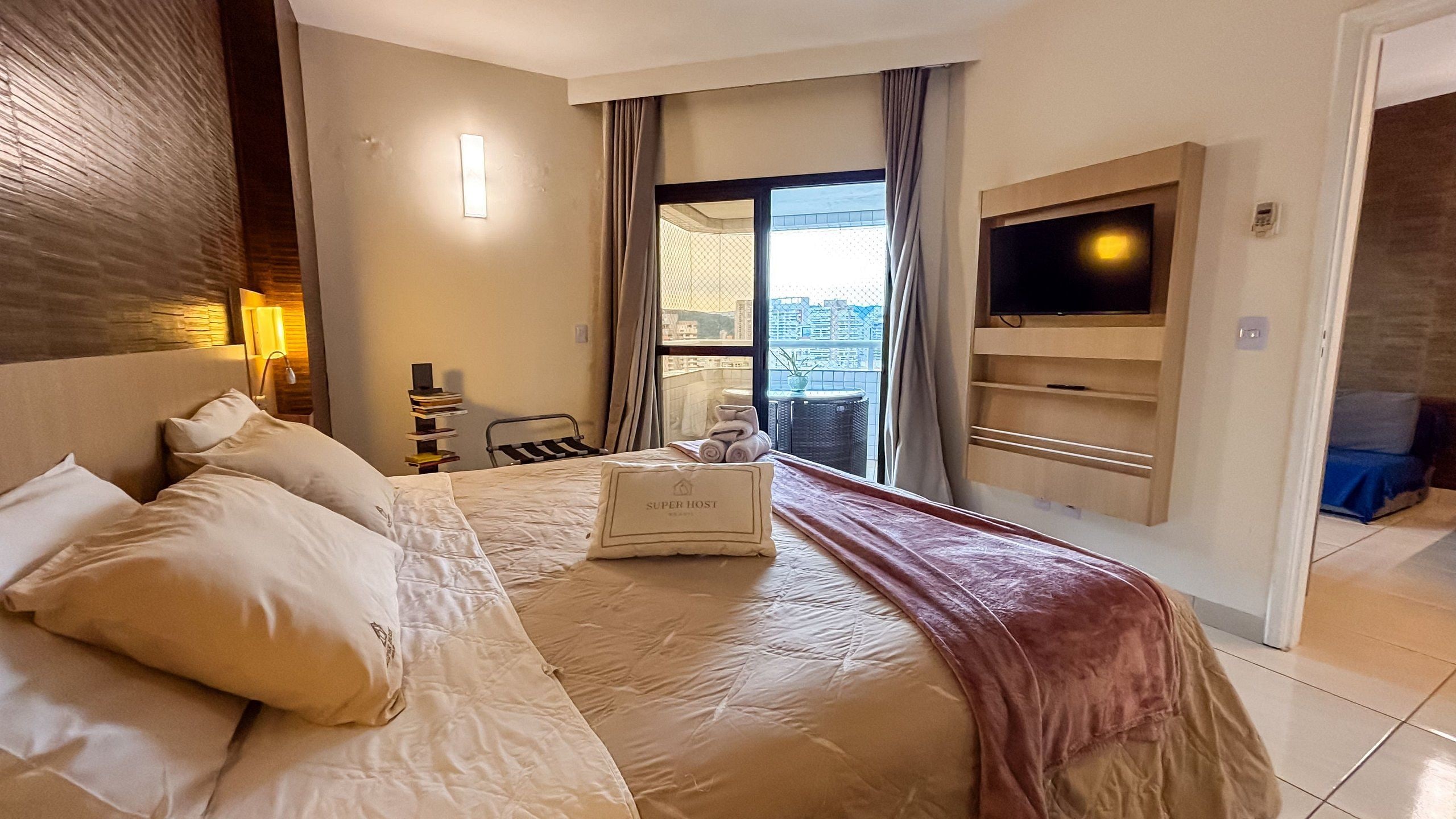 A hotel room with a large bed, a TV, a balcony with a view, and a desk with a chair.