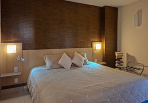 A neatly made bed with a quilted cover, two bedside lamps, a wooden headboard, and a small shelf with a book and a device. - SHB Magnífica vista ao mar em Santos (Santos)