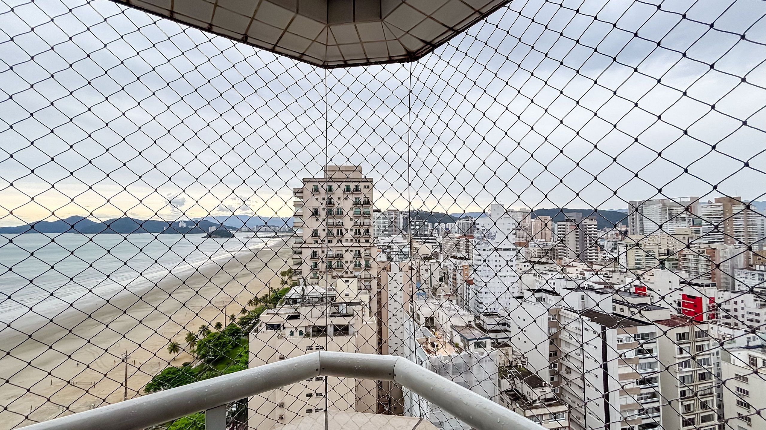 A chain-link fence overlooking a beach and a cityscape with high-rise buildings.