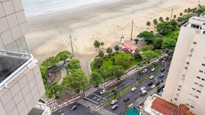 Un edifici alt amb vistes a una platja, palmeres i una carretera amb cotxes.