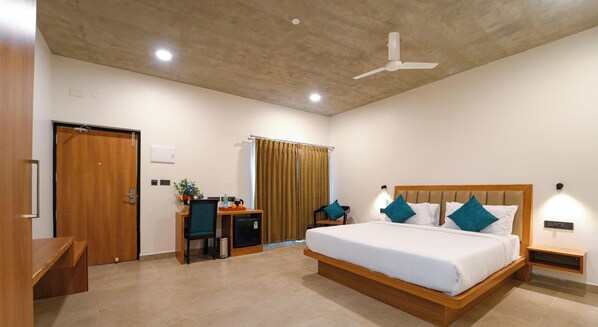 A hotel room with a bed, desk, chair, and a ceiling fan. - LEISURE RESORT (Vanur)