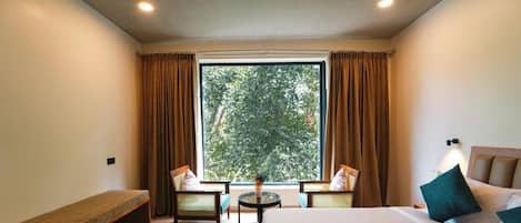 A hotel room with a bed, two chairs, a small table, and a window with curtains.