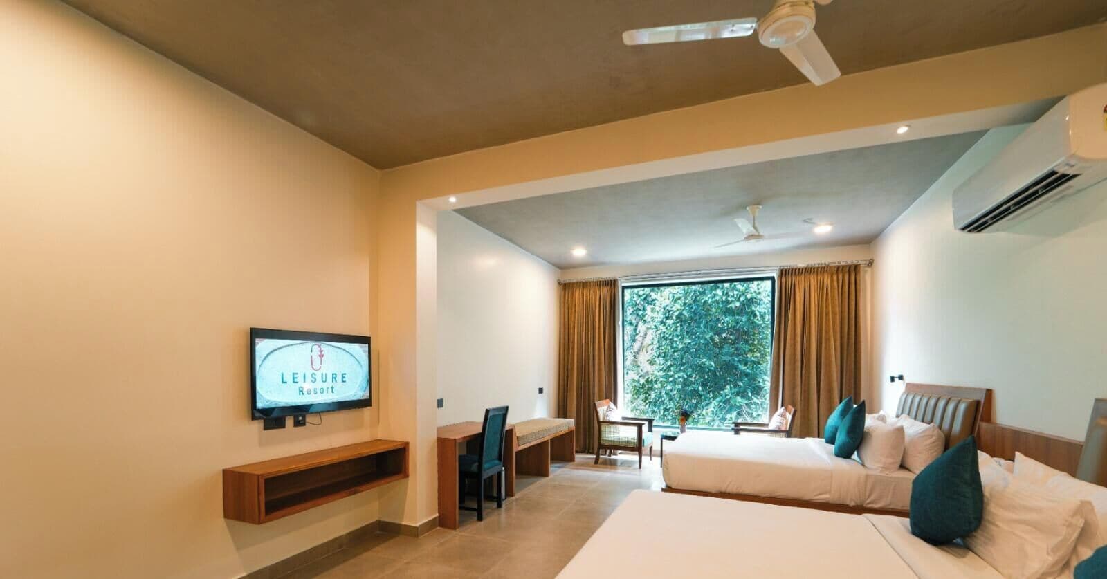 Habitación de hotel con cama, escritorio, silla, televisor y una ventana grande con cortinas.