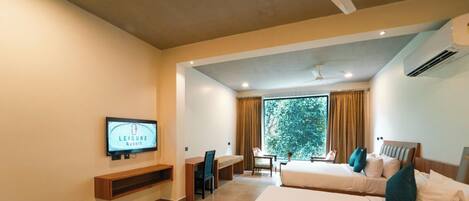 Habitación de hotel con cama, escritorio, silla, televisor y una ventana grande con cortinas.