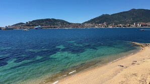 En kuststad med klart vatten, en sandstrand och ett berg i bakgrunden.
