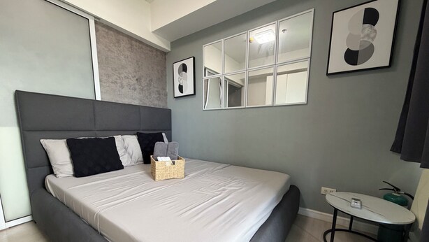 Quarto moderno com uma cama grande, uma mesinha de cabeceira, uma mesinha redonda e um espelho.