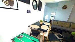 A living room with a pool table, a sofa, a dining table with chairs, and a small plant. - 2-bedroom Azure City and Beach View Condominium by JECstays (Parañaque)