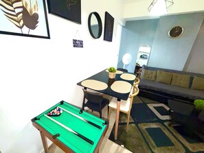 Ein Wohnzimmer mit Billardtisch, einer Couch, einem Esstisch mit Stühlen und einer kleinen Pflanze.