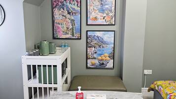 A child's room with a white crib, a small table with a bottle of hand sanitizer, and two framed paintings on the wall.