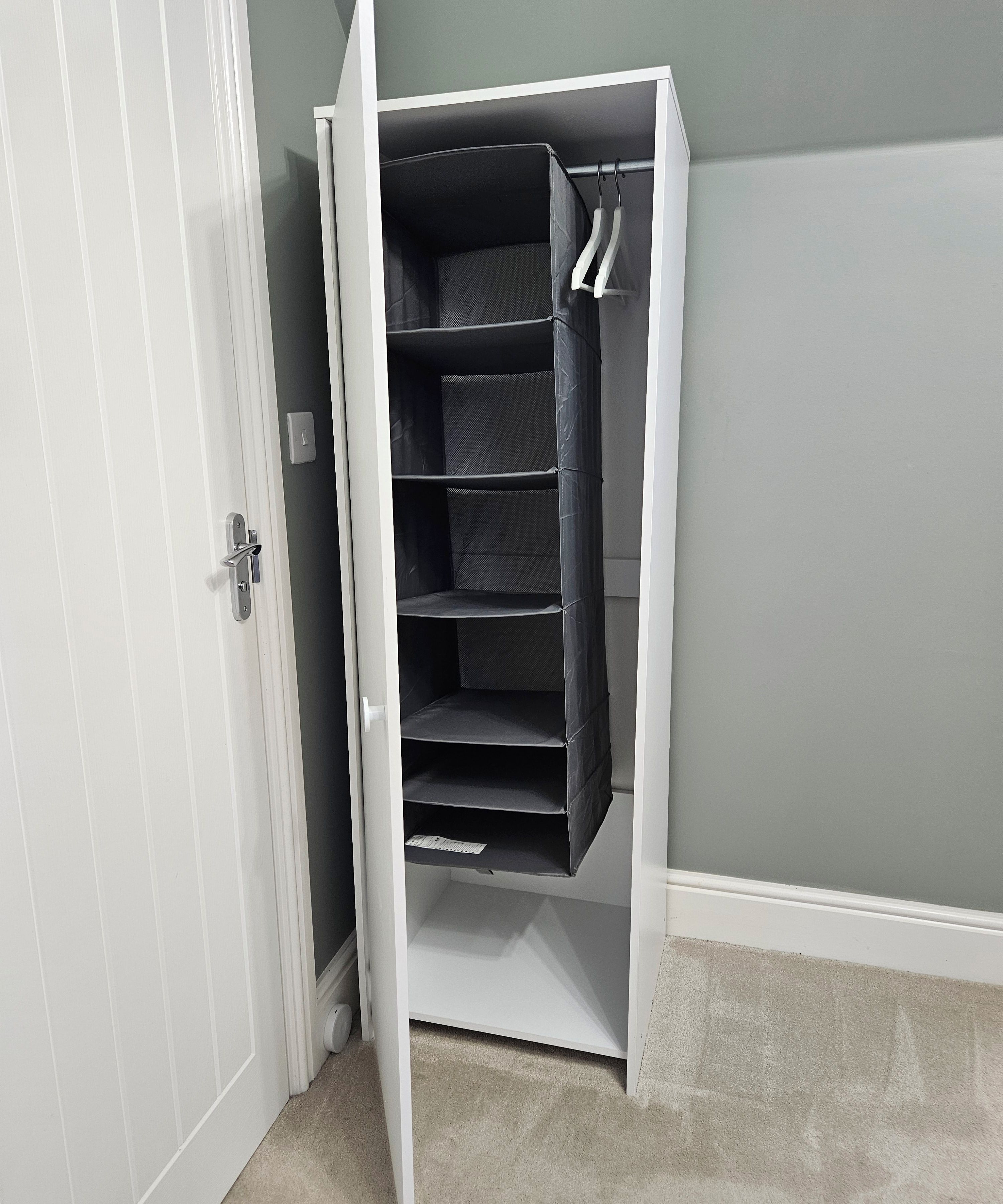 A white closet with multiple shelves and hanging space, positioned against a grey wall.