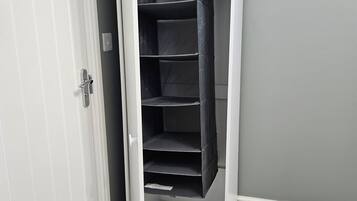 A white closet with multiple shelves and hanging space, positioned against a grey wall.