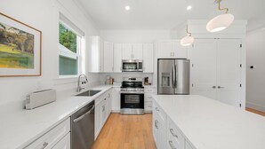 Una cocina moderna con armarios blancos, electrodomésticos de acero inoxidable e iluminación colgante.