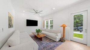 Ein modernes Wohnzimmer mit Flachbildfernseher, Deckenventilator, Sofa, Couchtisch und Lampe.