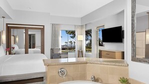 Habitación de hotel con una cama grande, baño con bañera, televisor montado en la pared y vistas a palmeras.