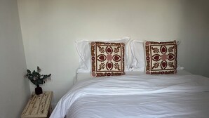 Ein Schlafzimmer mit einem großen Bett, zwei Zierkissen, einem kleinen Nachttisch mit Pflanze und einem Holzboden mit Fischgrätmuster.