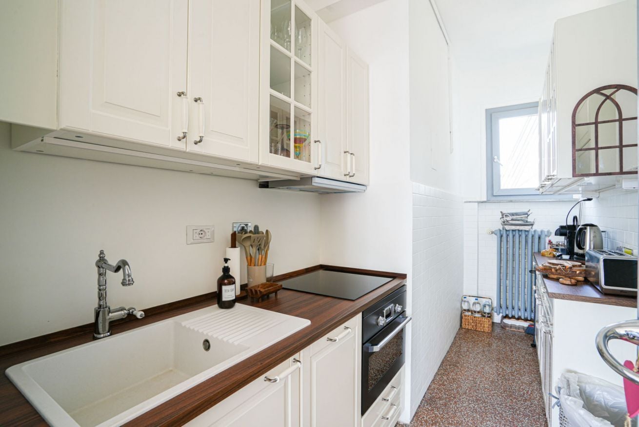 A compact kitchen with white cabinets, a stainless steel sink, a built-in oven, and a window providing natural light.