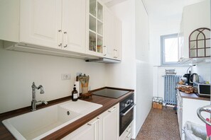 A compact kitchen with white cabinets, a stainless steel sink, a built-in oven, and a window providing natural light. - Piazza Statuto Terrace (Torino)