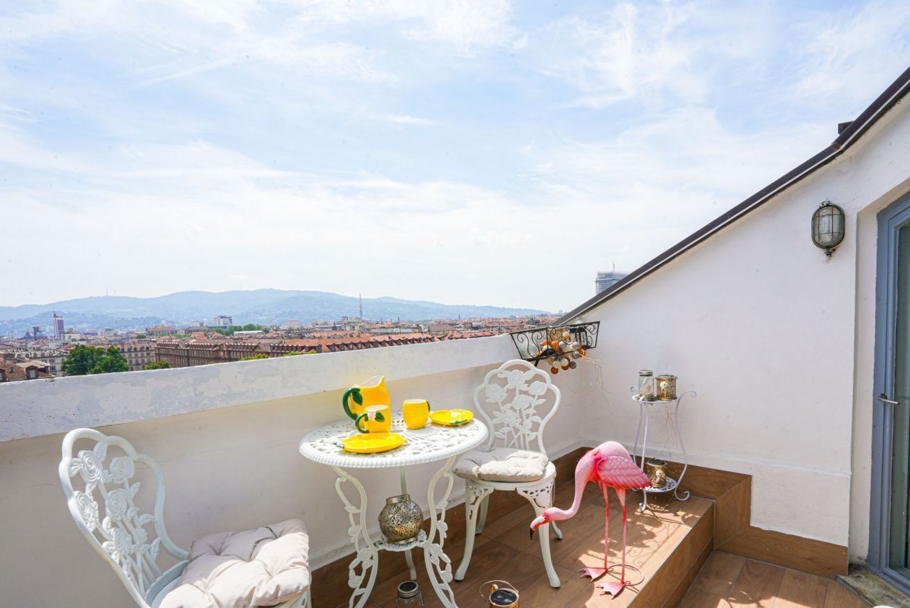 A balcony with a table, chairs, a pink flamingo decoration, and a view of a cityscape.