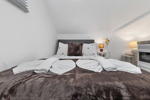 Ein modernes Schlafzimmer mit einem großen Bett, weißer Bettwäsche, einem braunen Fellüberwurf und einem Nachttisch mit Lampe und Vase.