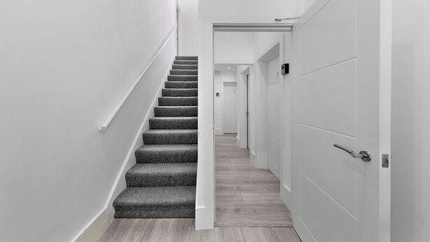 Un interior moderno con una escalera alfombrada que conduce a un pasillo con puertas blancas.