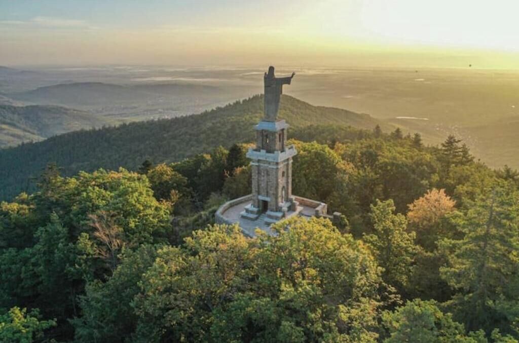 A monument surrounded by dense forest, with a panoramic view of distant hills.