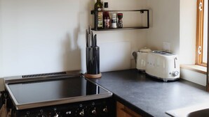 Een keuken met een zwarte kookplaat, een zwarte afzuigkap, houten kastjes, een zwarte messenhouder, een witte broodrooster en een plank met kruiden en specerijen.