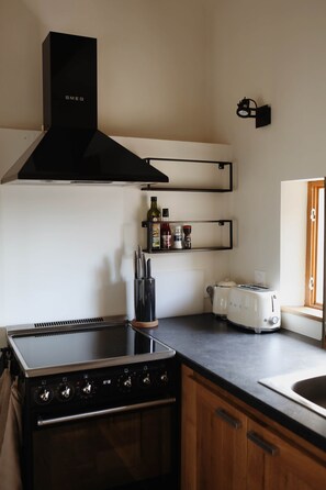 A kitchen with a black stove, a black range hood, wooden cabinets, a black knife block, a white toaster, and a shelf with condiments. - La Valette Boutique - La Grande Valette (Sanilhac-Sagriès)