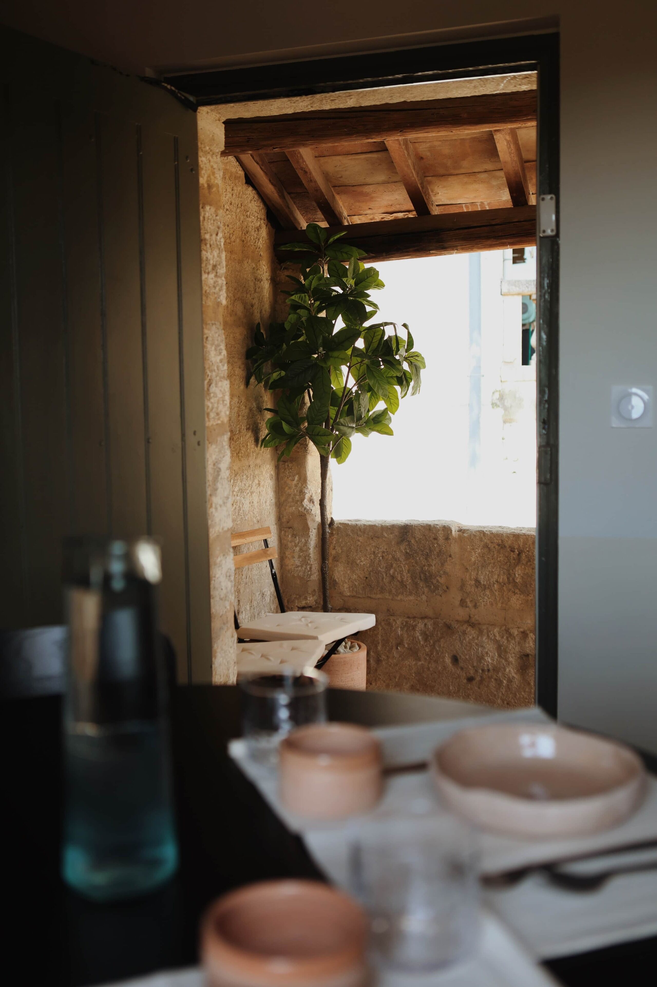 A rustic interior with a wooden table, a potted plant, and a view through an open doorway.