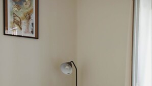 Een woonkamer met een bank, kussens, een vloerlamp en een ingelijst beeld aan de muur.