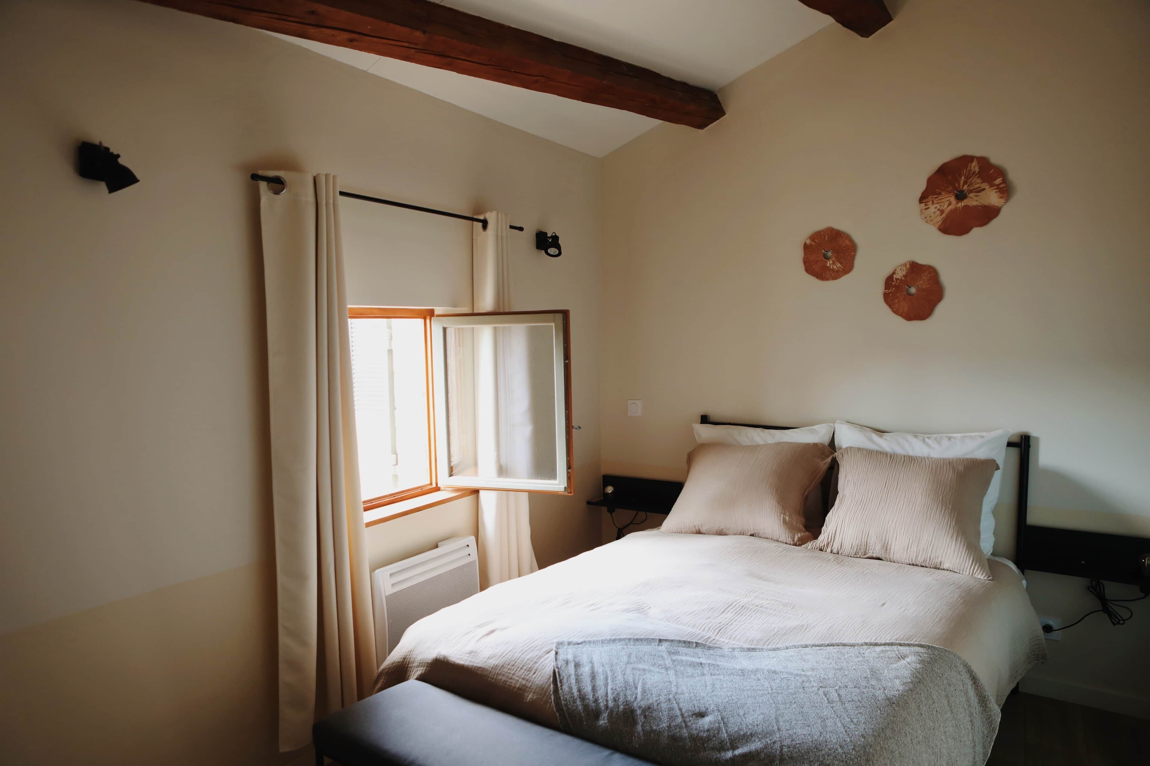 A bedroom with a bed, a window with curtains, a radiator, and wall decorations.