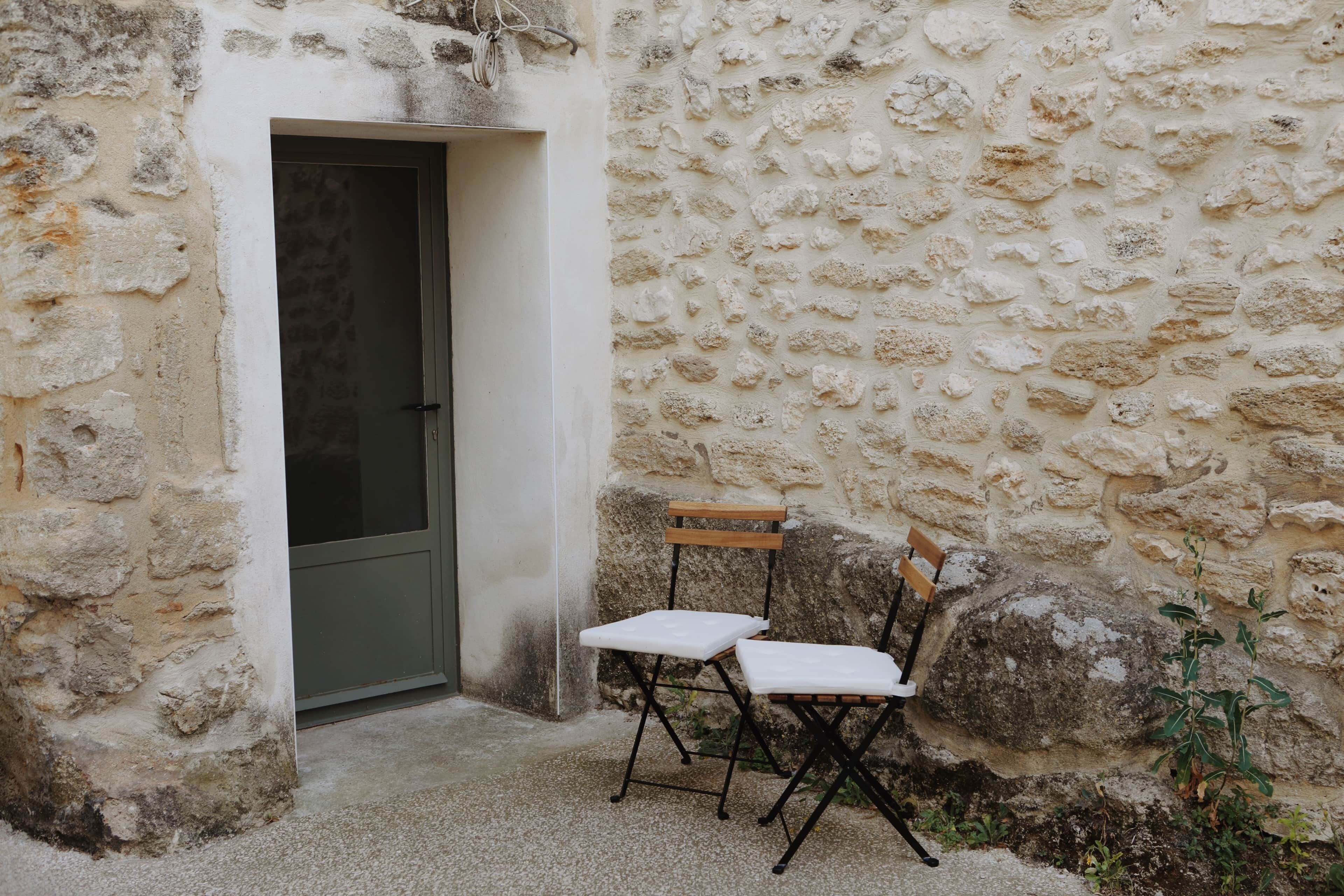 A stone wall, a door, and two white folding chairs.