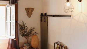 Una habitación con techo de madera, una mesa con un jarrón, un estante de pared con libros y una lámpara colgante.