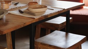 Una mesa de comedor con fuentes, vasos y cubiertos, un banco y una lámpara fijada a la pared.