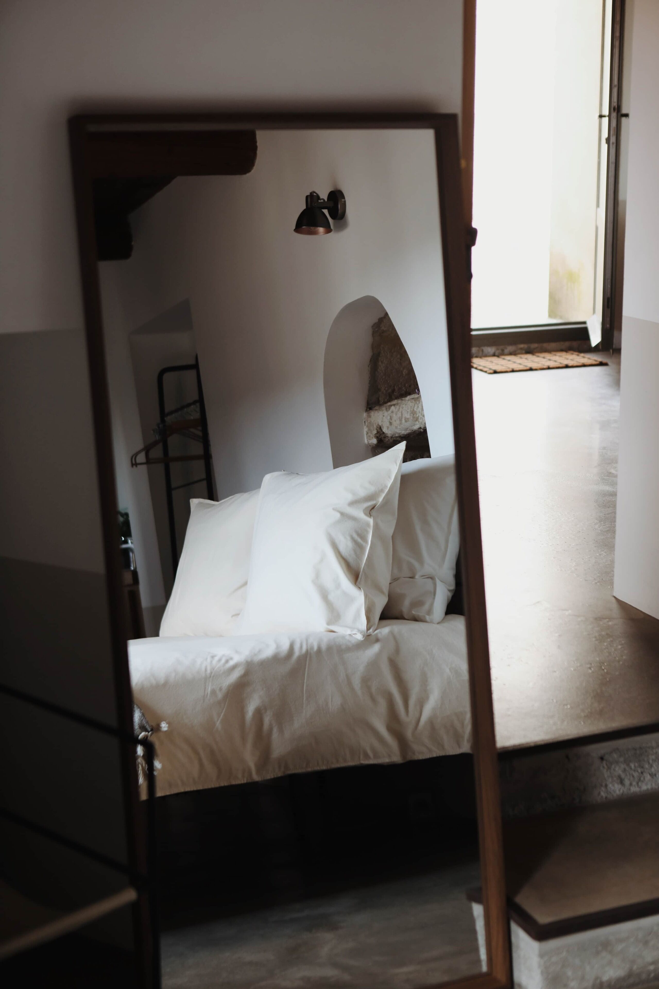 Un lit avec une literie blanche, une tête de lit en bois et une petite fenêtre donnant sur un paysage agréable.