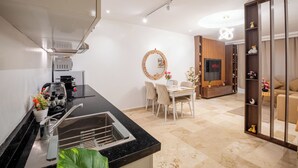 Eine moderne Küche mit Einbauherd, ein Essbereich mit rundem Holztisch und Stühlen, sowie ein Wohnbereich mit Sofa und Fernseher.