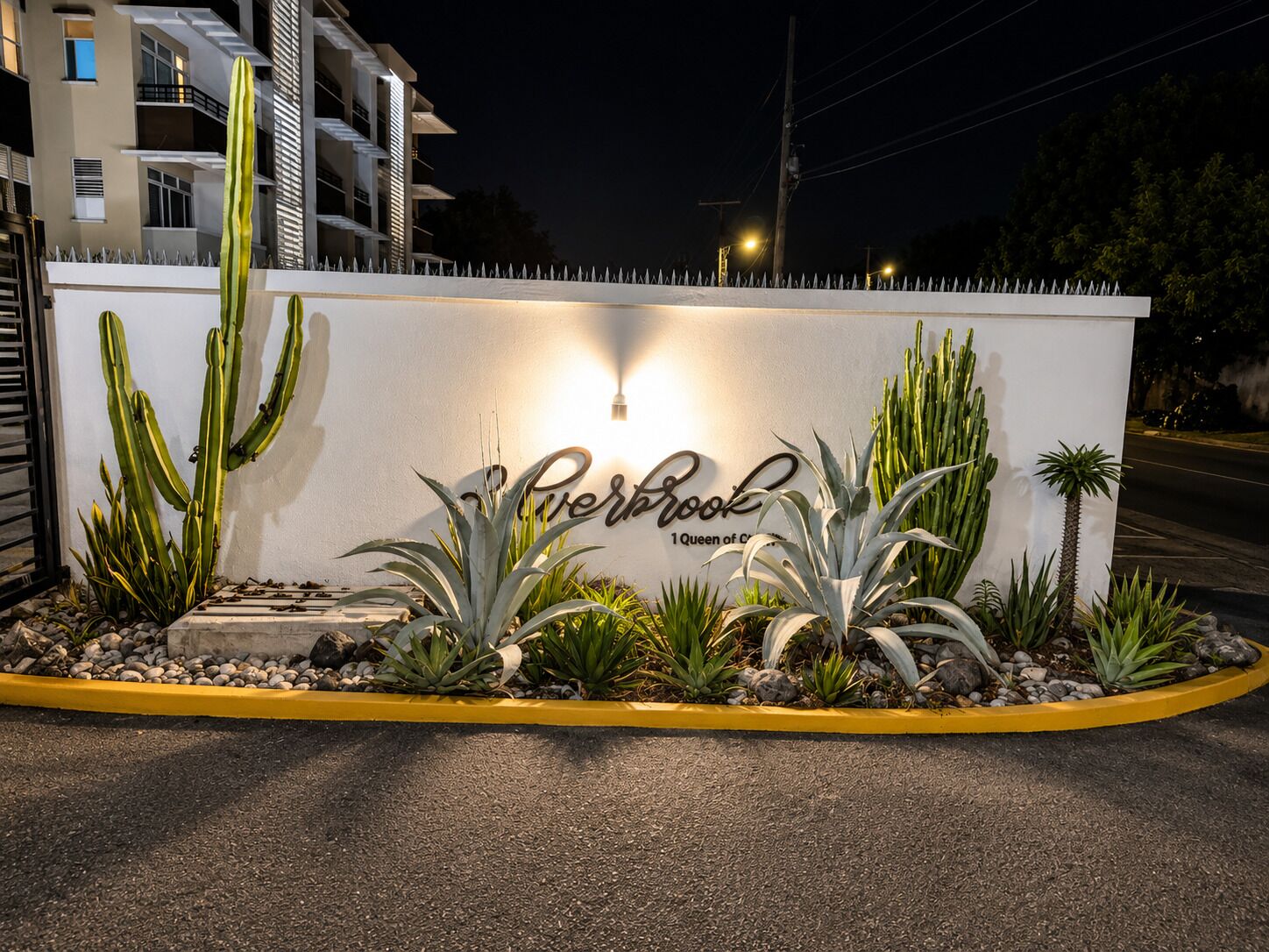 A hotel entrance with a white wall, cacti, and a sign that reads 'Perbrook 1 Queen of the Caribbean.'
