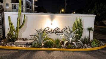 A hotel entrance with a white wall, cacti, and a sign that reads 'Perbrook 1 Queen of the Caribbean.'