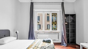 A bedroom with a bed, a radiator, a window with curtains, and a view of buildings outside. - MO10 Pleasant Stay x4 in Milan (Milano)