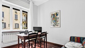 A room with a dining table, chairs, a TV, a colorful abstract painting, and a window with a view of buildings. - MO10 Pleasant Stay x4 in Milan (Milano)