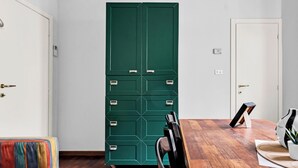 A room with a wooden floor, a green storage unit with multiple drawers, a white door, and a colorful chair. - MO10 Pleasant Stay x4 in Milan (Milano)